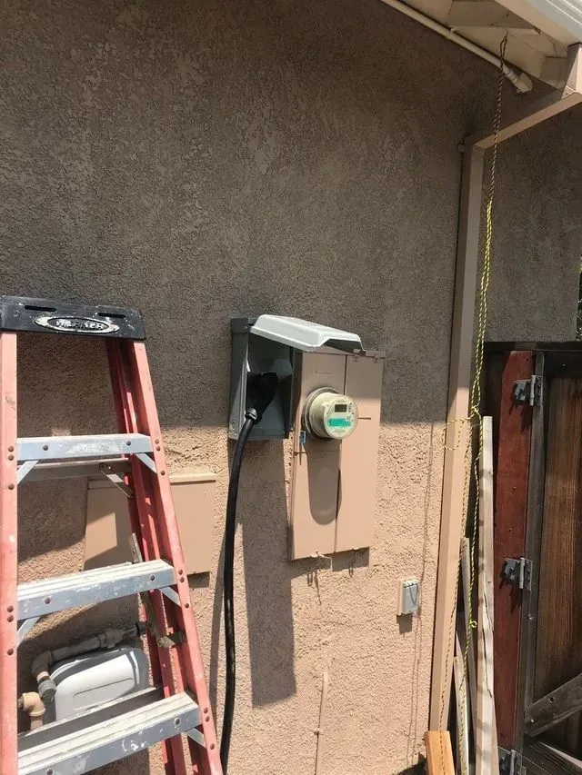 Ladder beside an exterior wall with electric meter and conduit under a roof overhang
