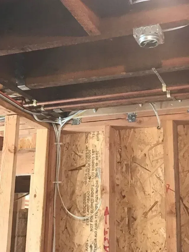 Exposed ceiling joists and wiring in a framed construction area with an open garage door opener.