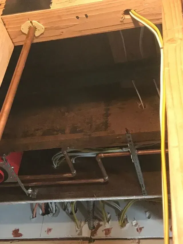 Open wall cabinet with a metal shelf and hanging yellow cable under wooden beams
