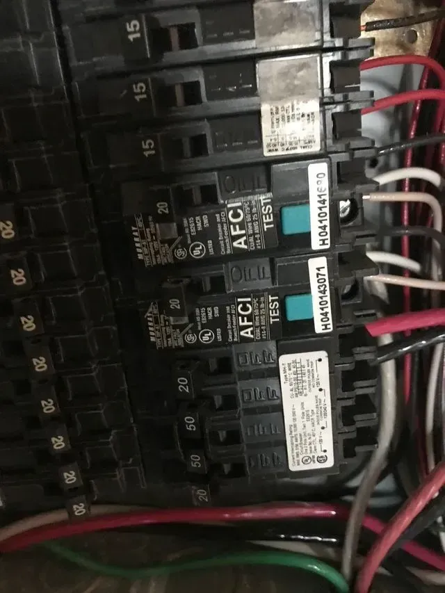 Electrical circuit breaker panel with labeled black breakers, red and white wires, and a green wire at the bottom