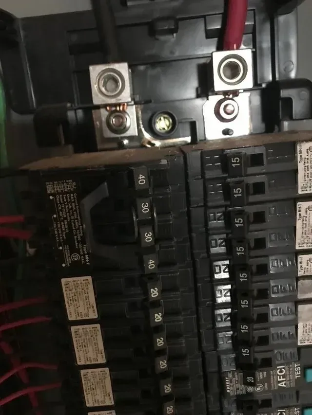 Close-up of an electrical breaker panel with rows of black switches and heavy red wires.