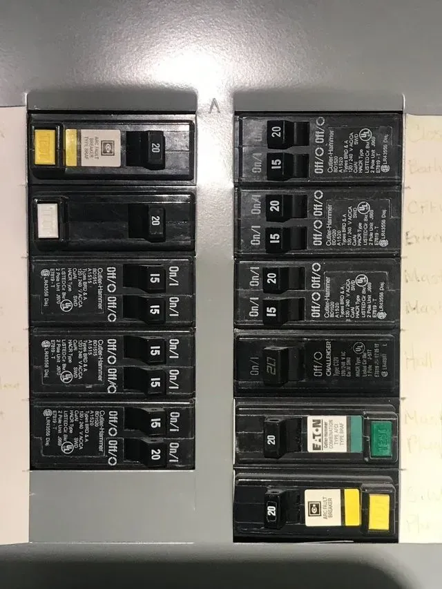 Electrical breaker panel with black circuit breakers and two colored switches, viewed inside a metal box