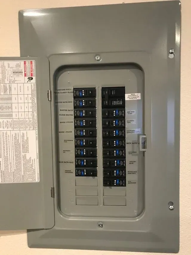 Open electrical breaker panel with rows of black circuit switches on a gray wall.
