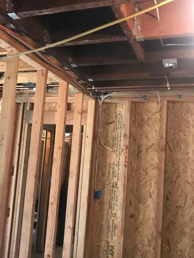 Exposed wooden framing and ceiling joists inside a room under construction, with a hanging wire.