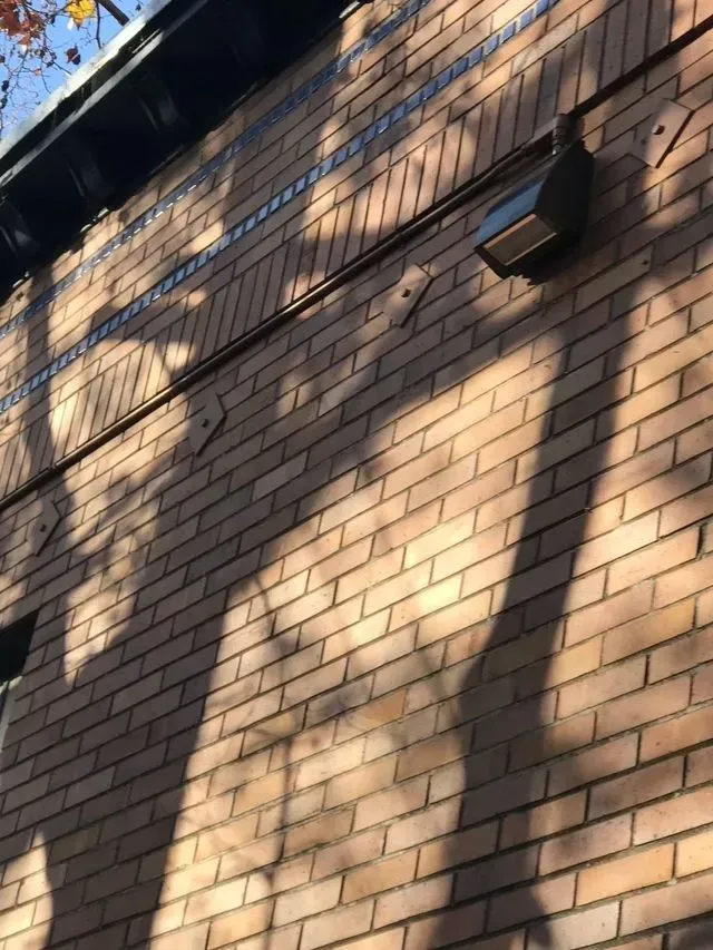 Brick building wall with diagonal sunlight and shadow patterns, plus a mounted outdoor light fixture.