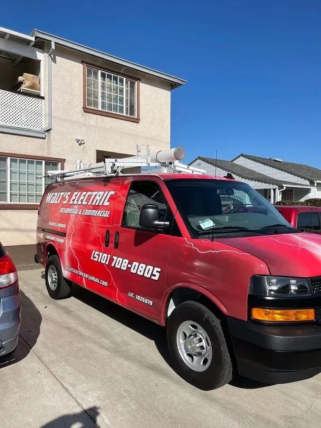 Red electric service van parked on a residential street beside a house, with company logo and phone number on the side