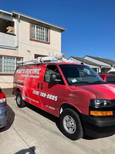 Red commercial van parked in a suburban driveway beside a house, with ladder racks on top.