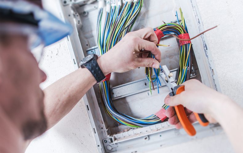 Electrician wiring a breaker panel with colored cables and orange wire cutters