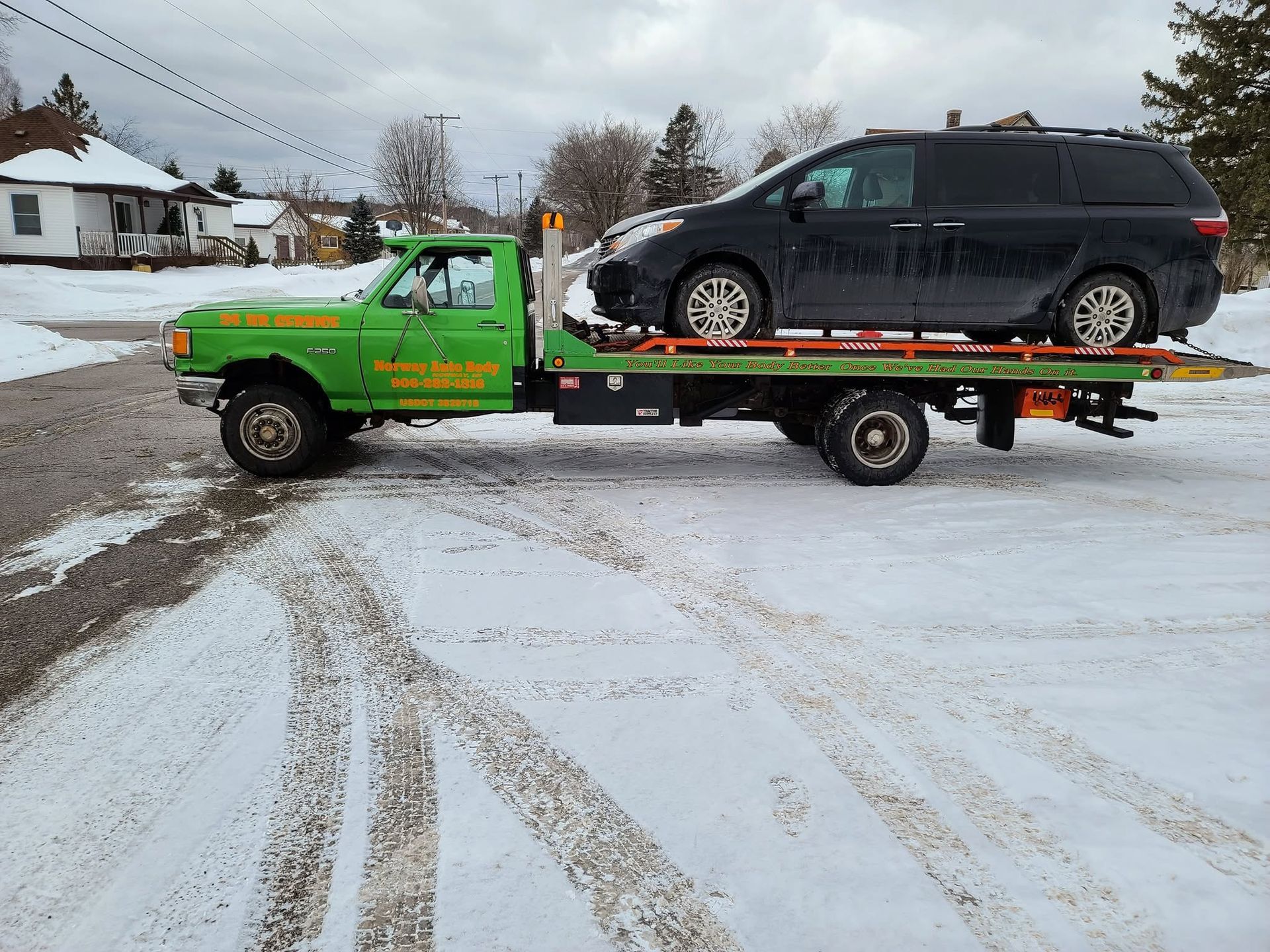 Green tow truck carrying a black SUV on a snowy street