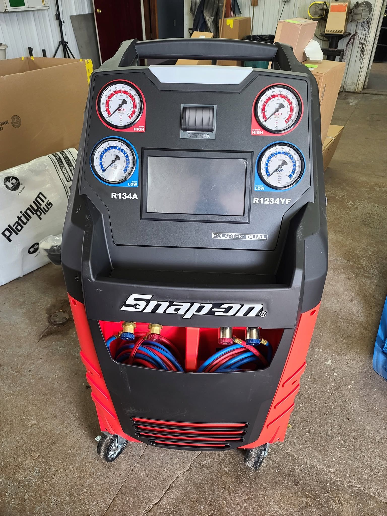 Snap-on automotive A/C service machine with gauges and red lower panel on a shop floor
