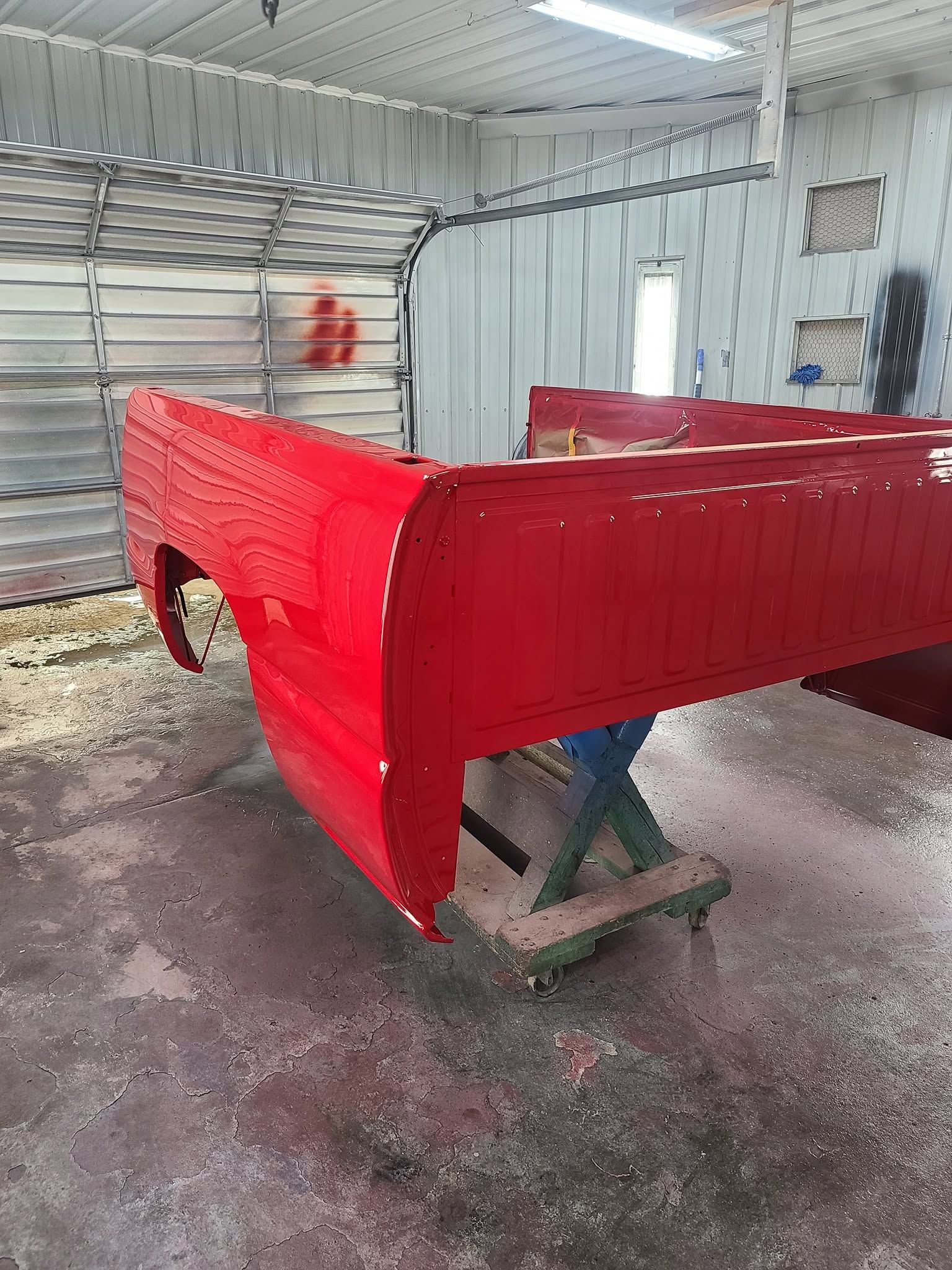 Red vehicle body shell in a workshop, freshly painted and resting on a stand.