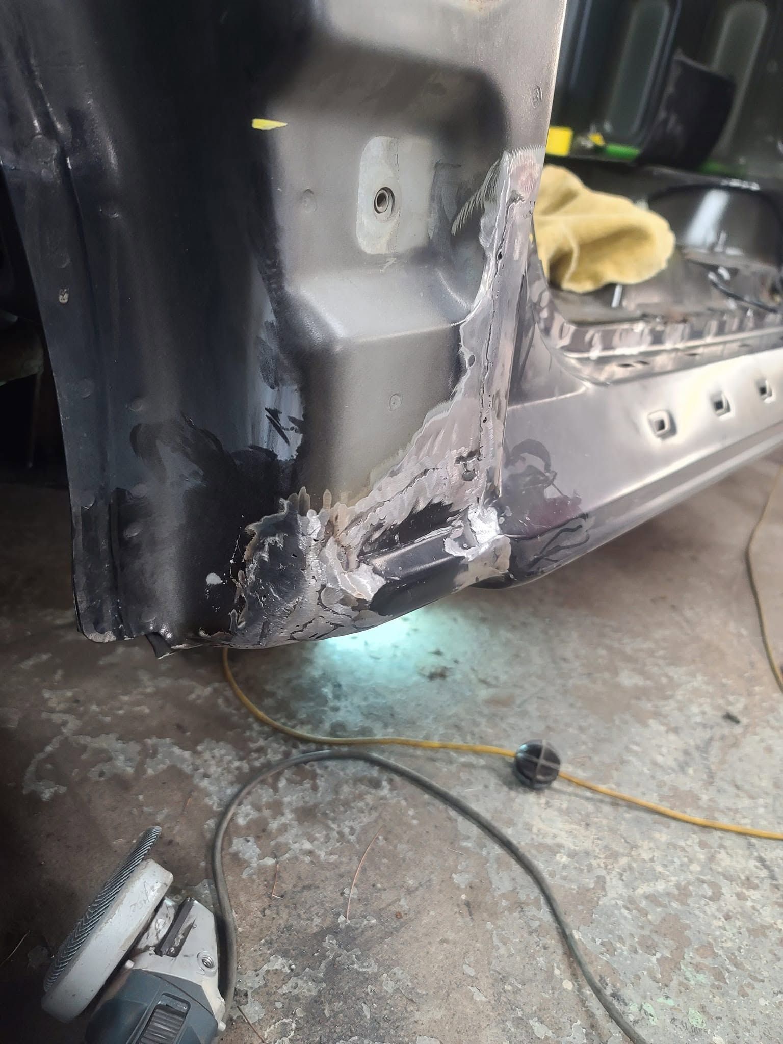 Severely damaged car door sill with melted metal and debris near the ground in a workshop