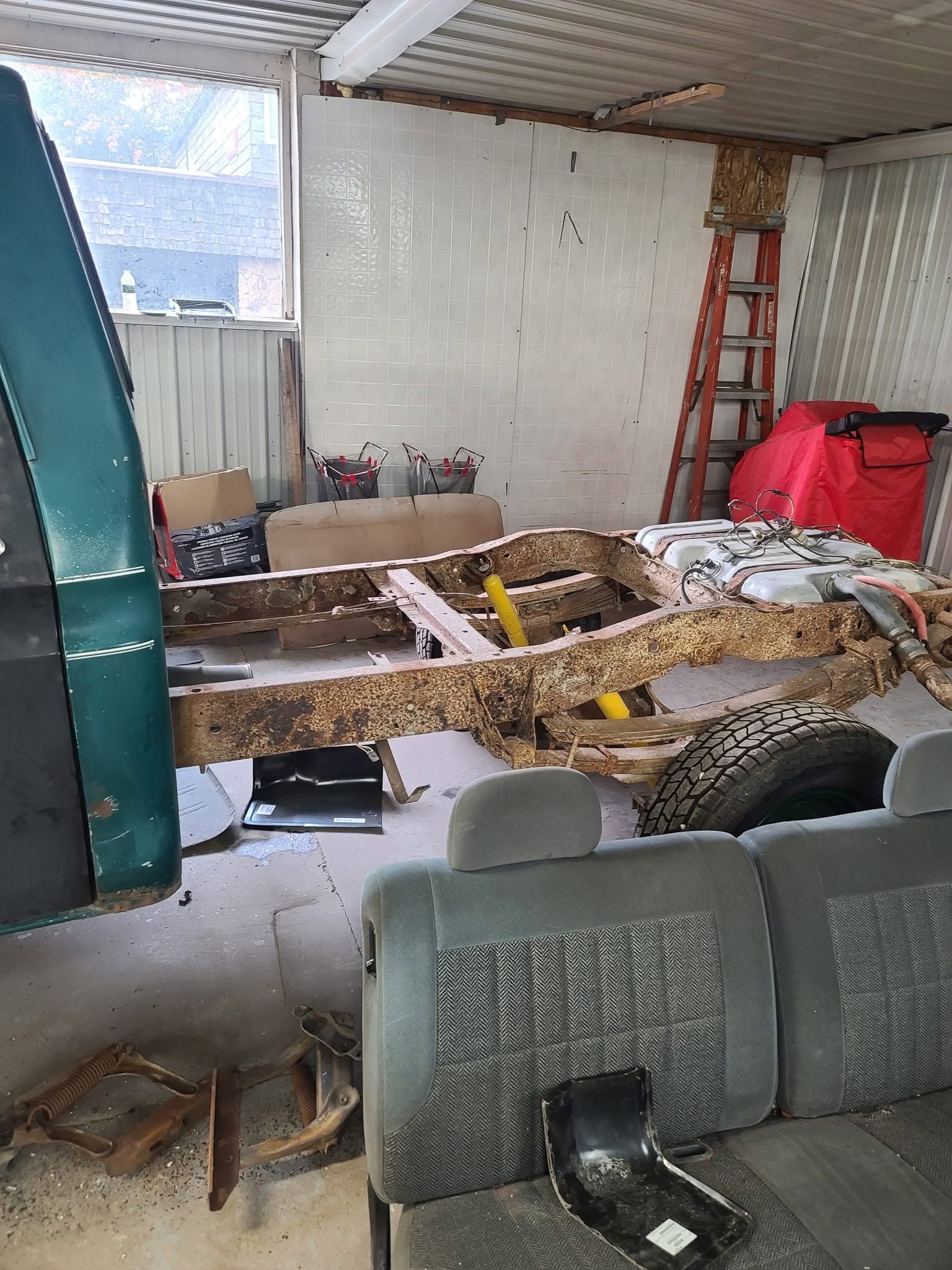 Damaged interior with broken floor, exposed dirt, a red ladder, and construction debris near a covered patio