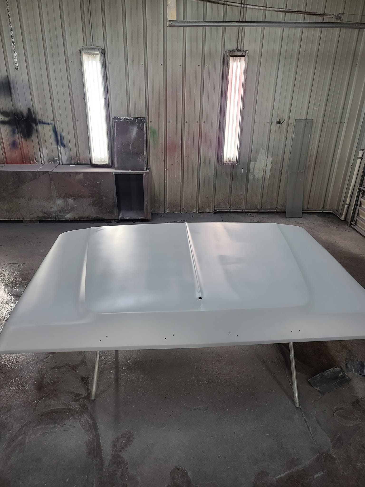 White car hood in a workshop, with two fluorescent lights reflected on its glossy surface.