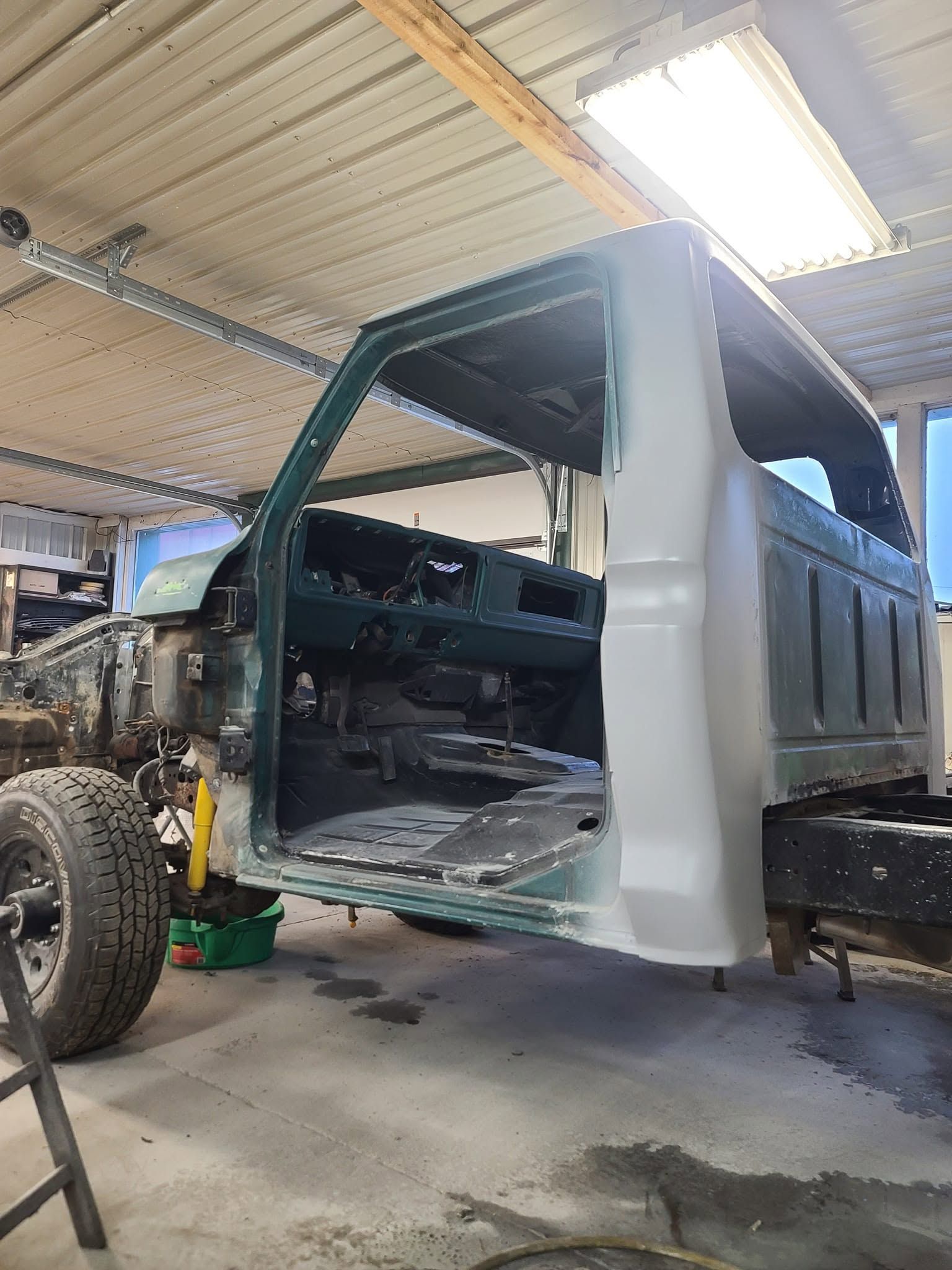 Partially disassembled dark green pickup truck in a repair shop under bright overhead lights
