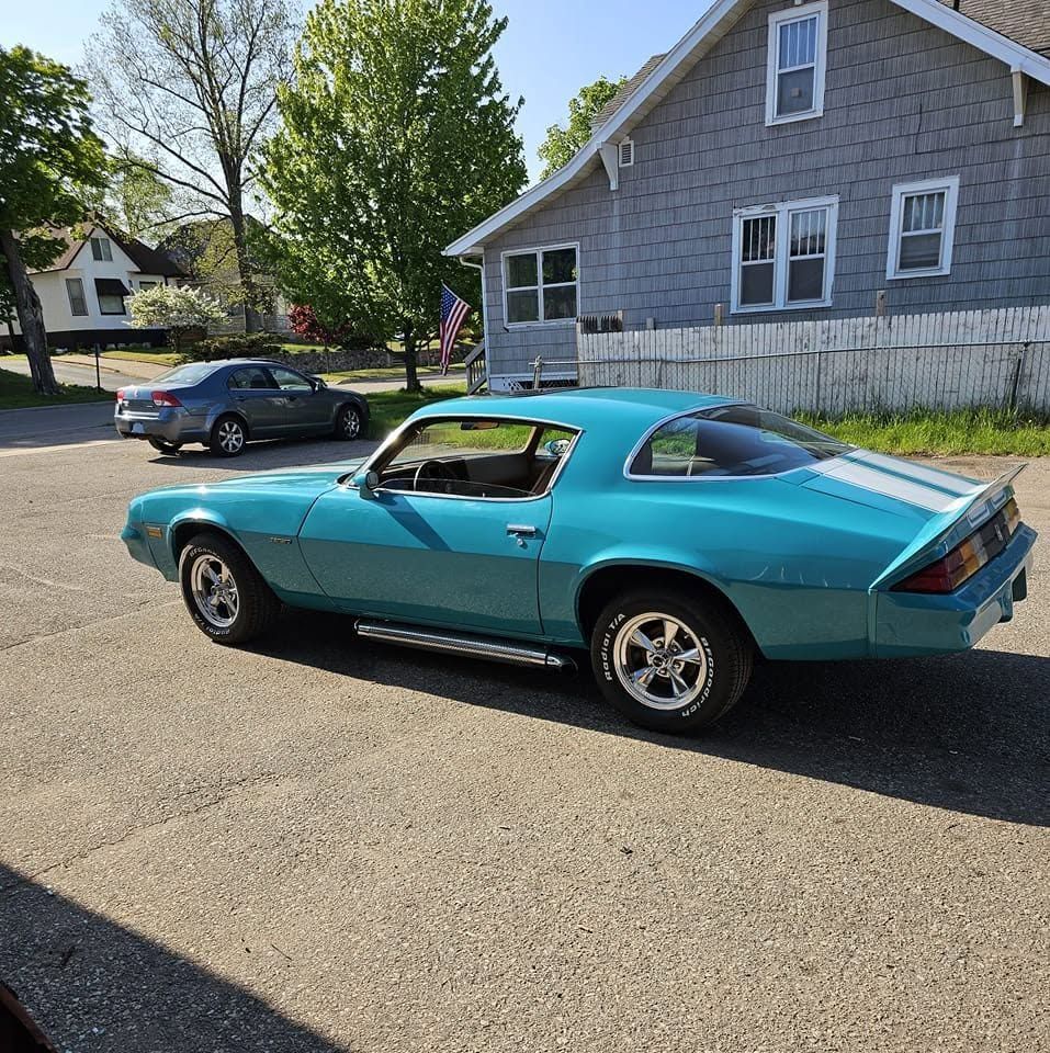 Turquoise classic muscle car parked on a residential street beside a gray house.