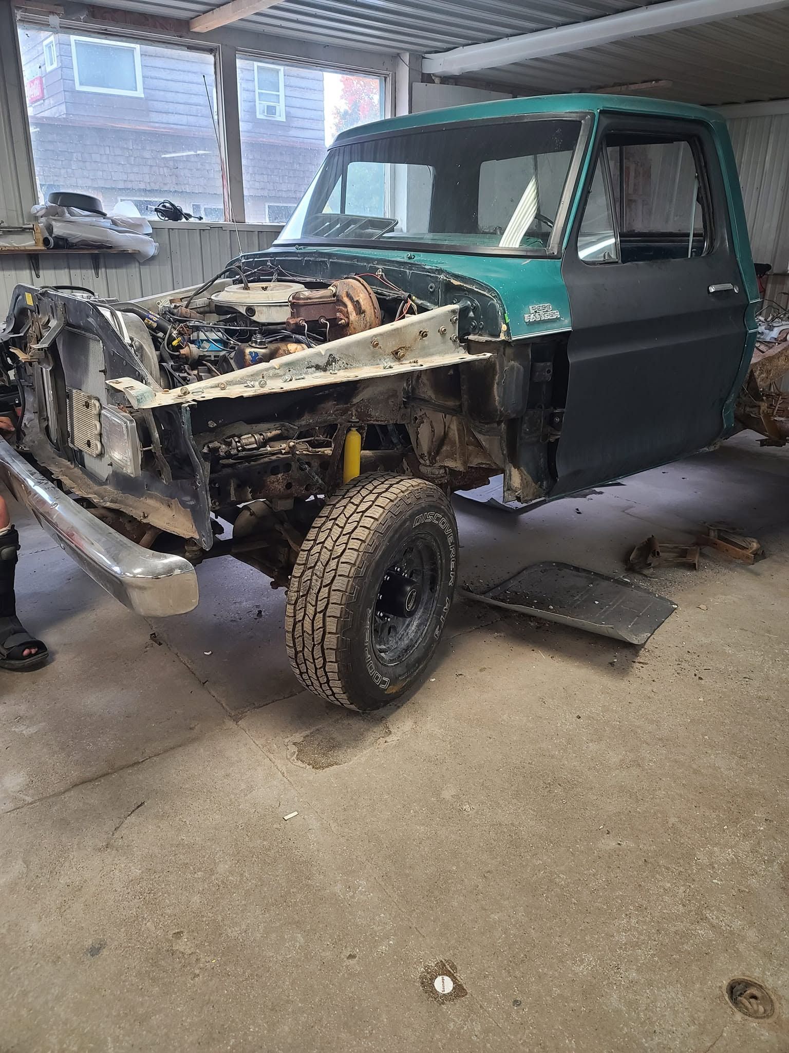 Partially disassembled teal pickup truck in a garage with the front end removed and exposed engine bay