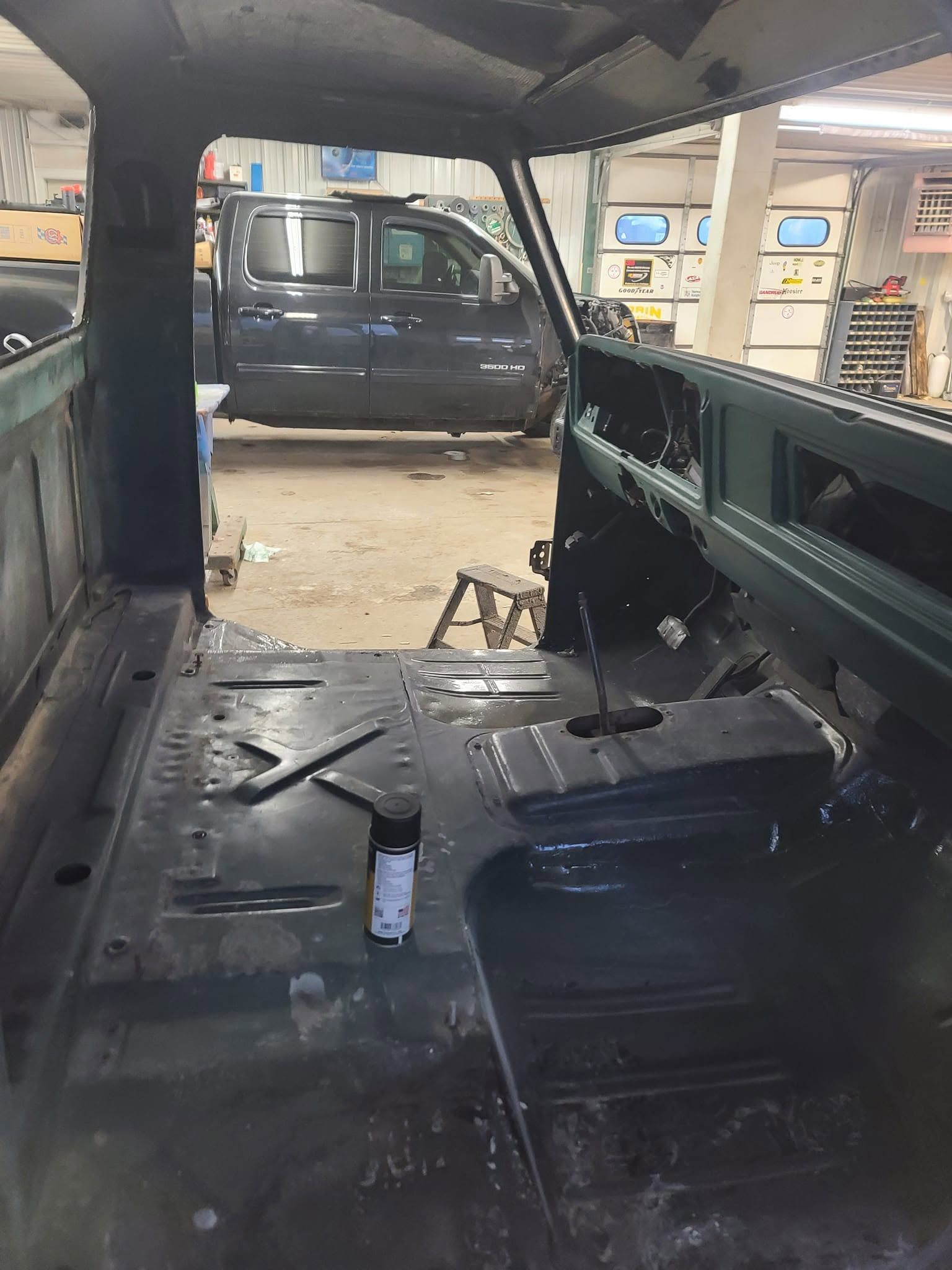 Interior of a stripped vehicle shell in a garage, with bare metal floor and missing seats and trim.