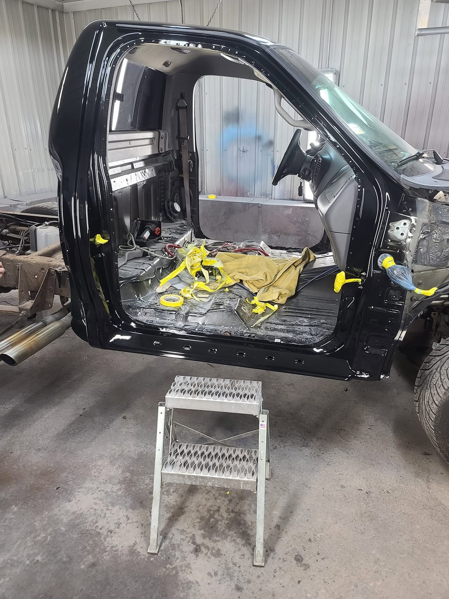 Black vehicle body shell in a workshop, with exposed interior and a stool in front