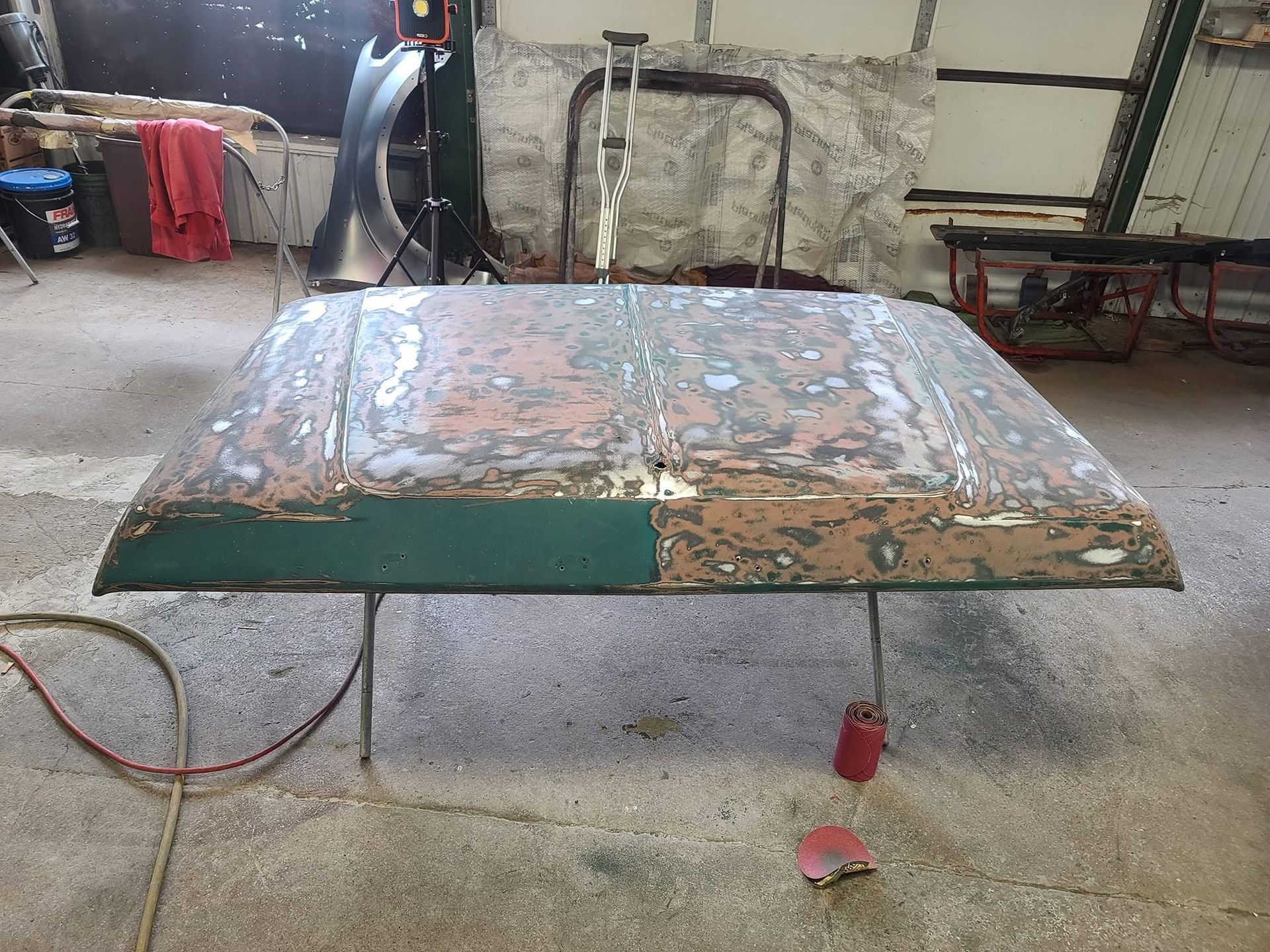 Rusty metal table panel in a workshop, with a green edge and a red cable on the concrete floor.
