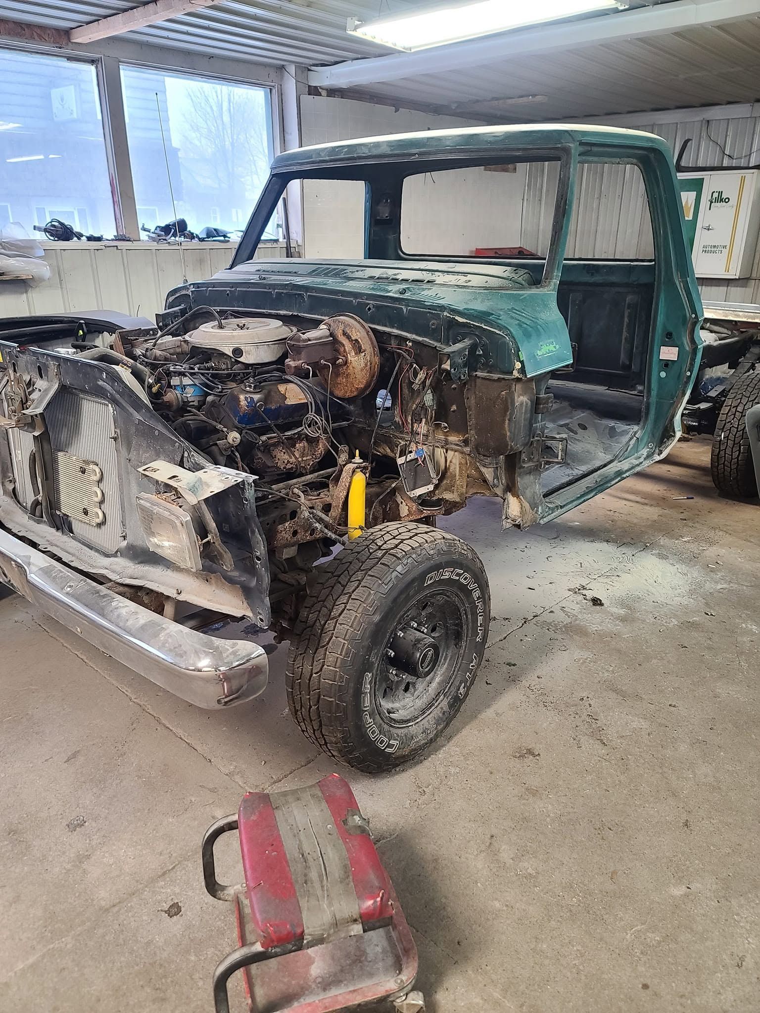 Damaged green SUV with front end removed in a workshop, exposing engine and frame.