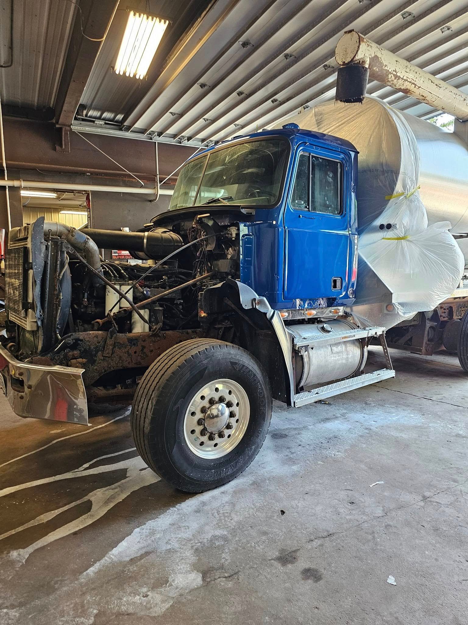 Blue truck cab with exposed front end and white mixer drum inside a garage