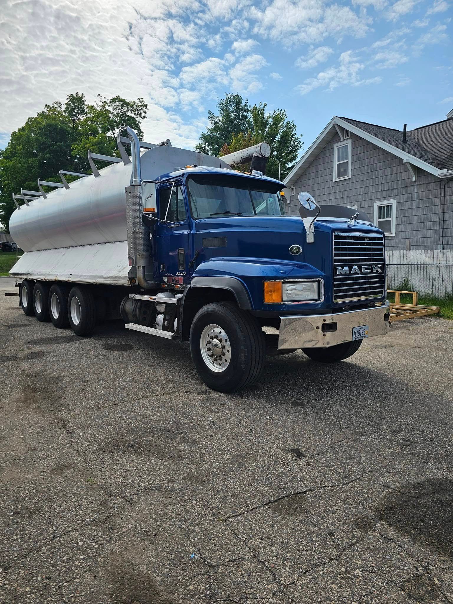 Blue dump truck with a silver trailer parked on a gravel driveway beside a house