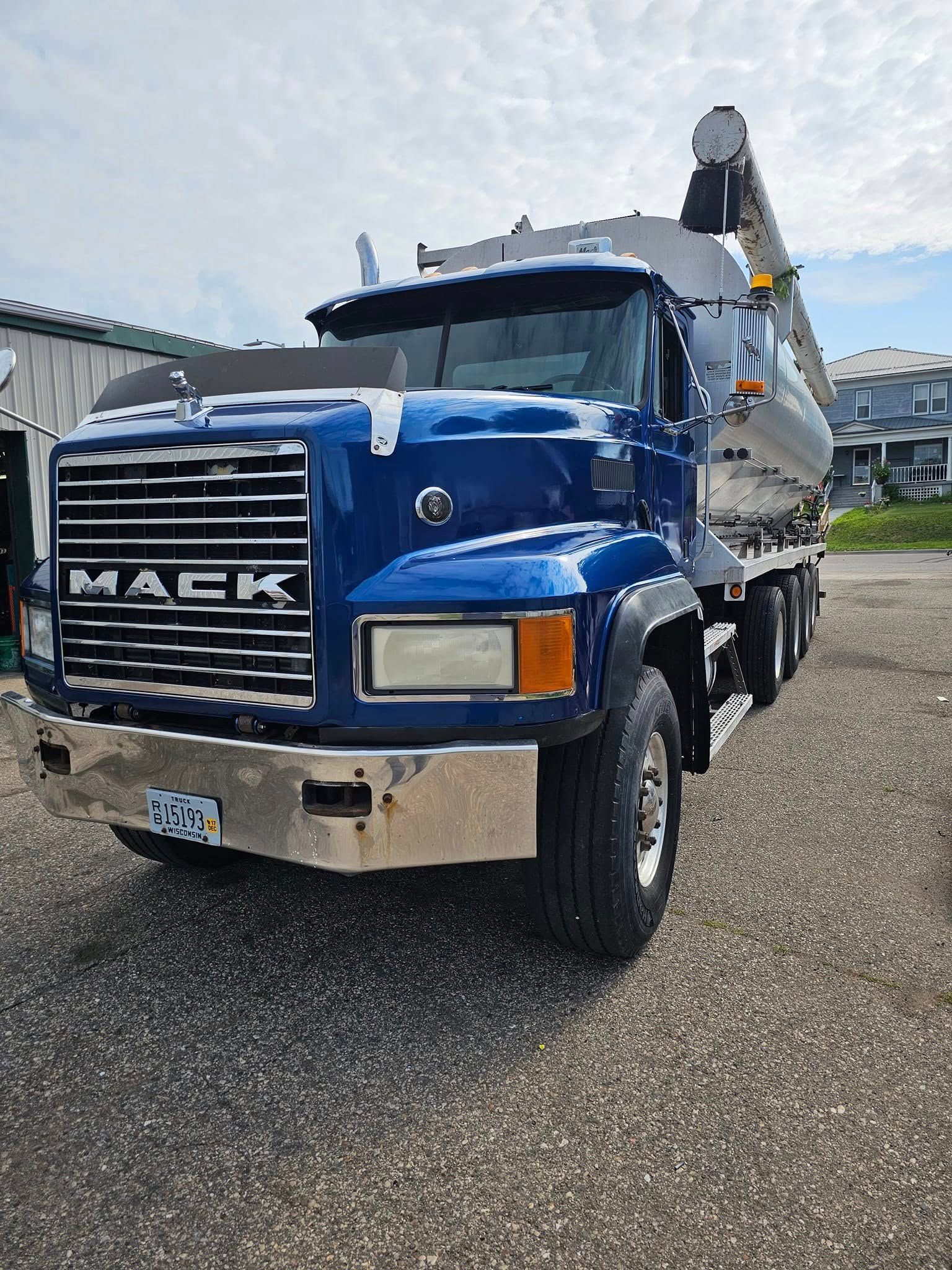 Blue Mack dump truck parked on wet pavement in a yard, front-left view