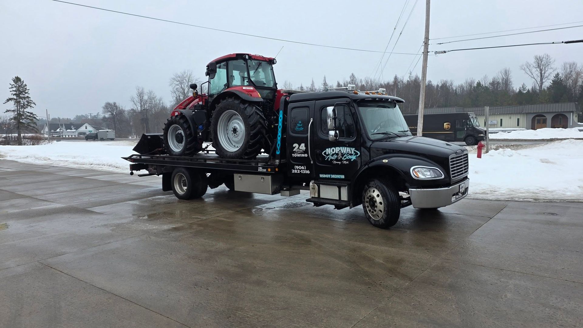 Tow truck carrying a red tractor on a snowy roadside
