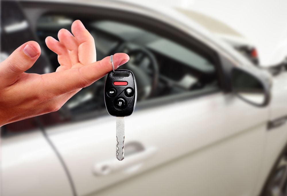 Hand Holding a Car Key Fob in Front of a White Car — Battery Assist Brisbane in Bribie Island, QLD