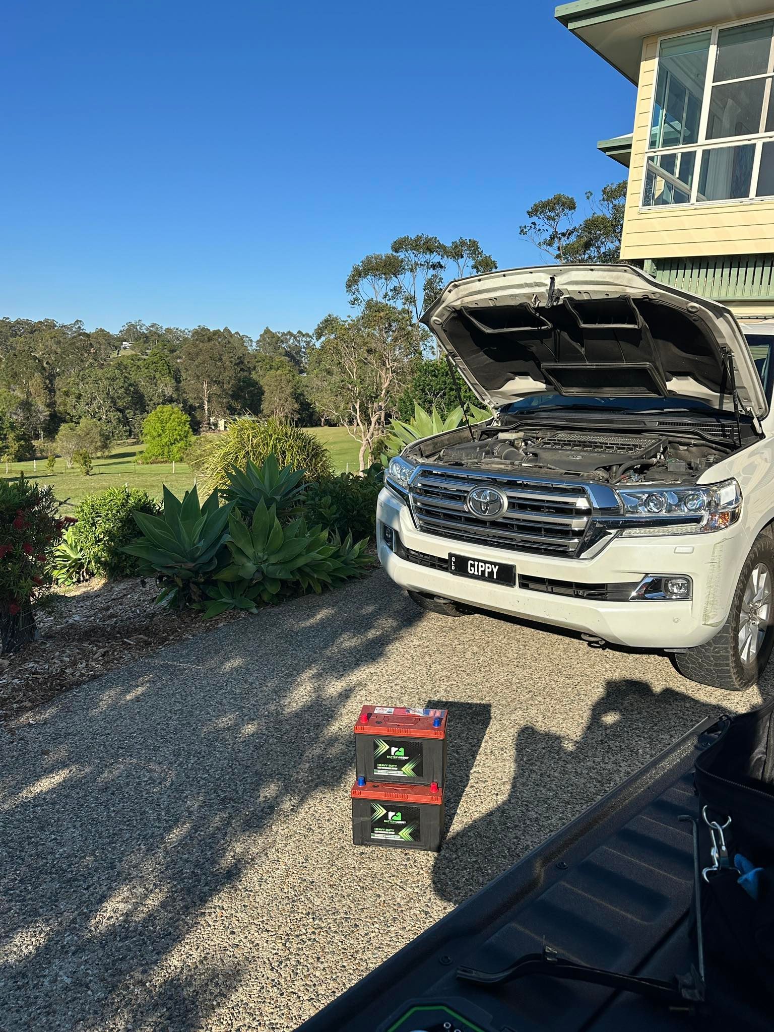 White SUV With Hood Open on a Gravel Driveway Beside a House — Battery Assist Brisbane in Ascot, QLD