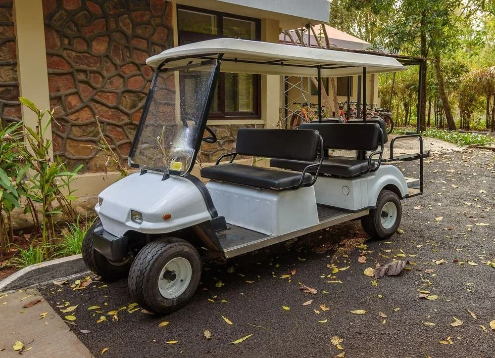 White Golf Cart Parked on Asphalt Near a Stone Building and Trees — Battery Assist Brisbane in Caboolture, QLD