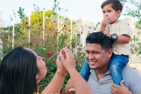 Family in a garden: two adults and a child smiling while looking at a tiny object together