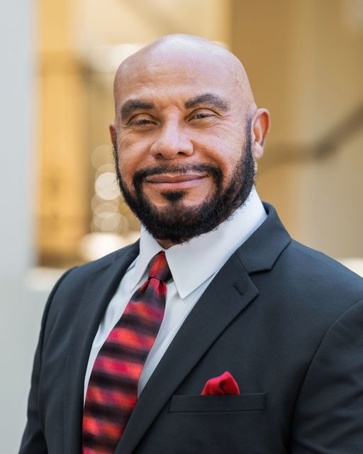 Smiling man in a dark suit with a red-and-black striped tie and red pocket square
