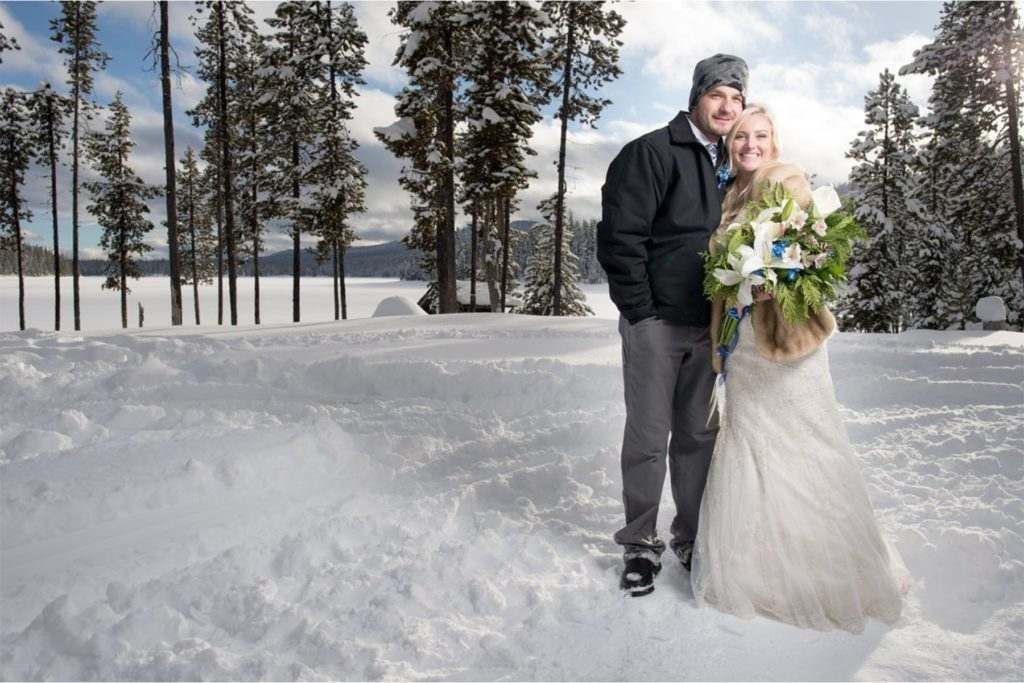 A bride and groom are posing for a picture in the snow.
