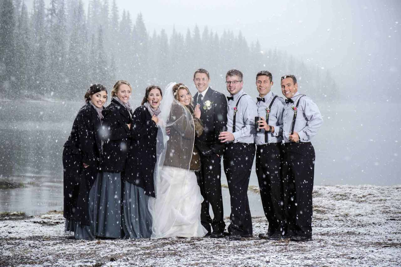 A bride and groom are posing for a picture with their wedding party in the snow.