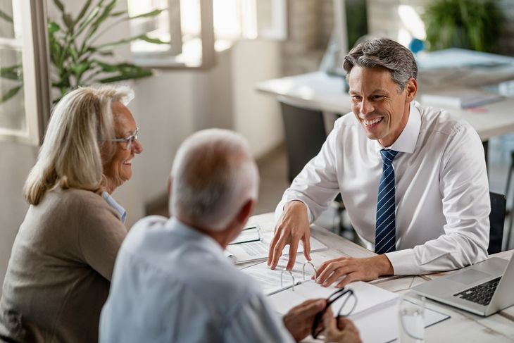 Three people in a meeting, discussing documents at a desk in a bright office.