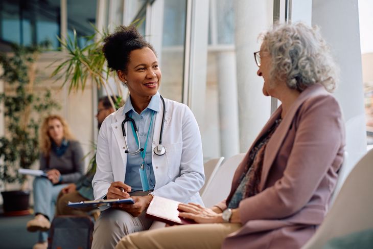 Two people talking in a bright waiting area, one holding a clipboard and smiling.