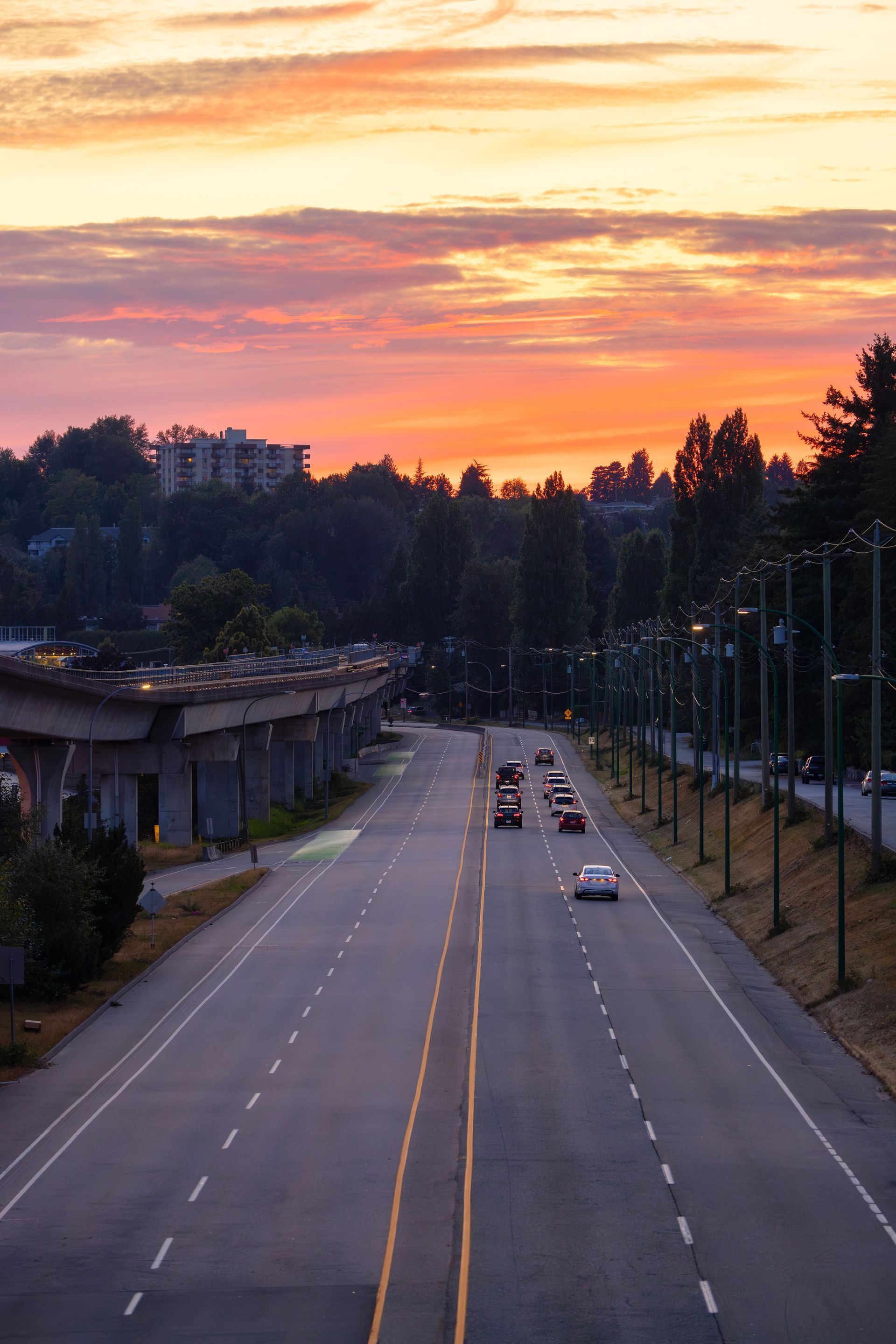 Sunset over a mostly empty city road with a few cars and trees lining the sides