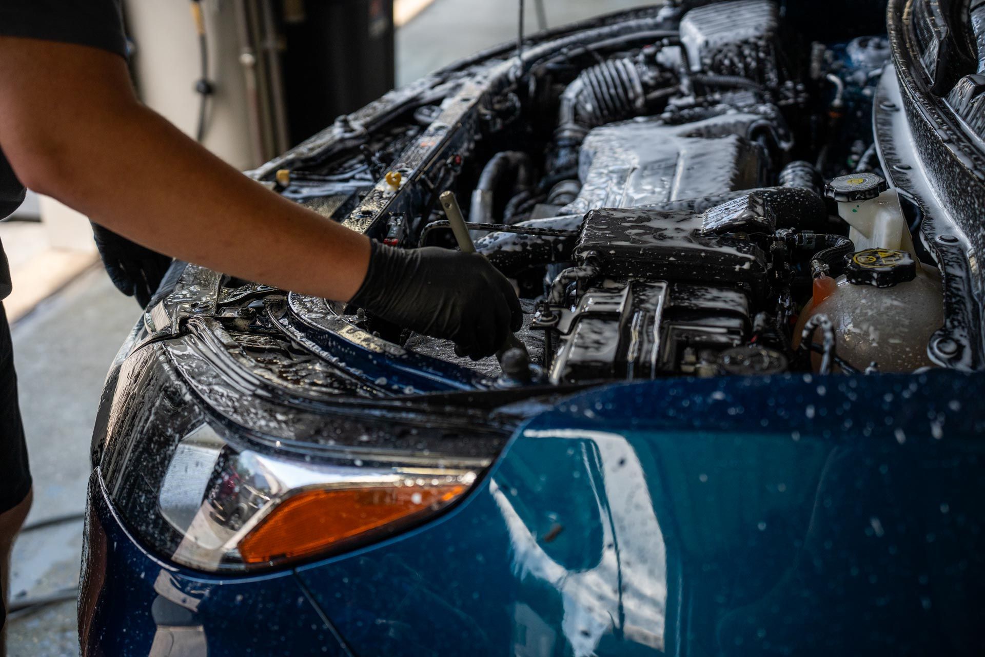 A man is cleaning the engine of a blue car.