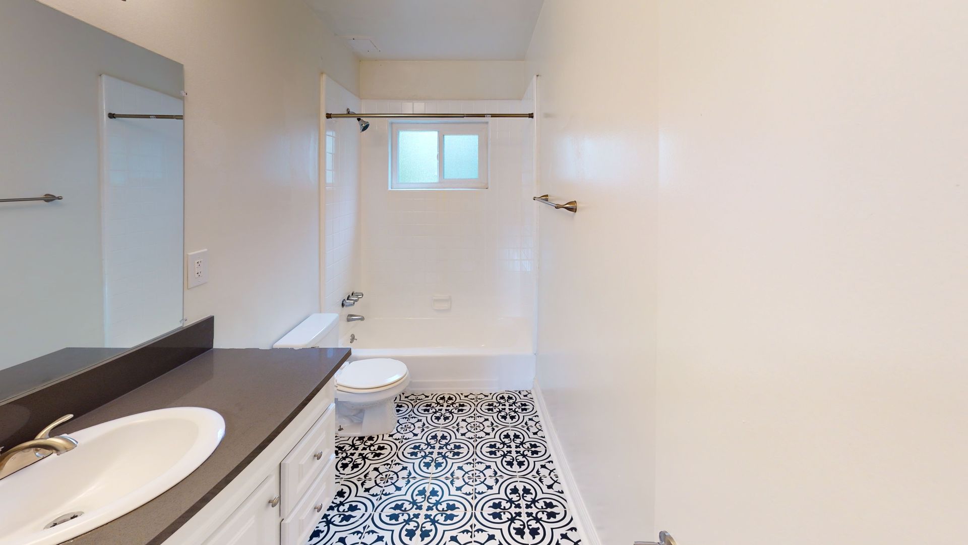 Bathroom with white walls, patterned floor, tub, toilet, vanity, and small window.