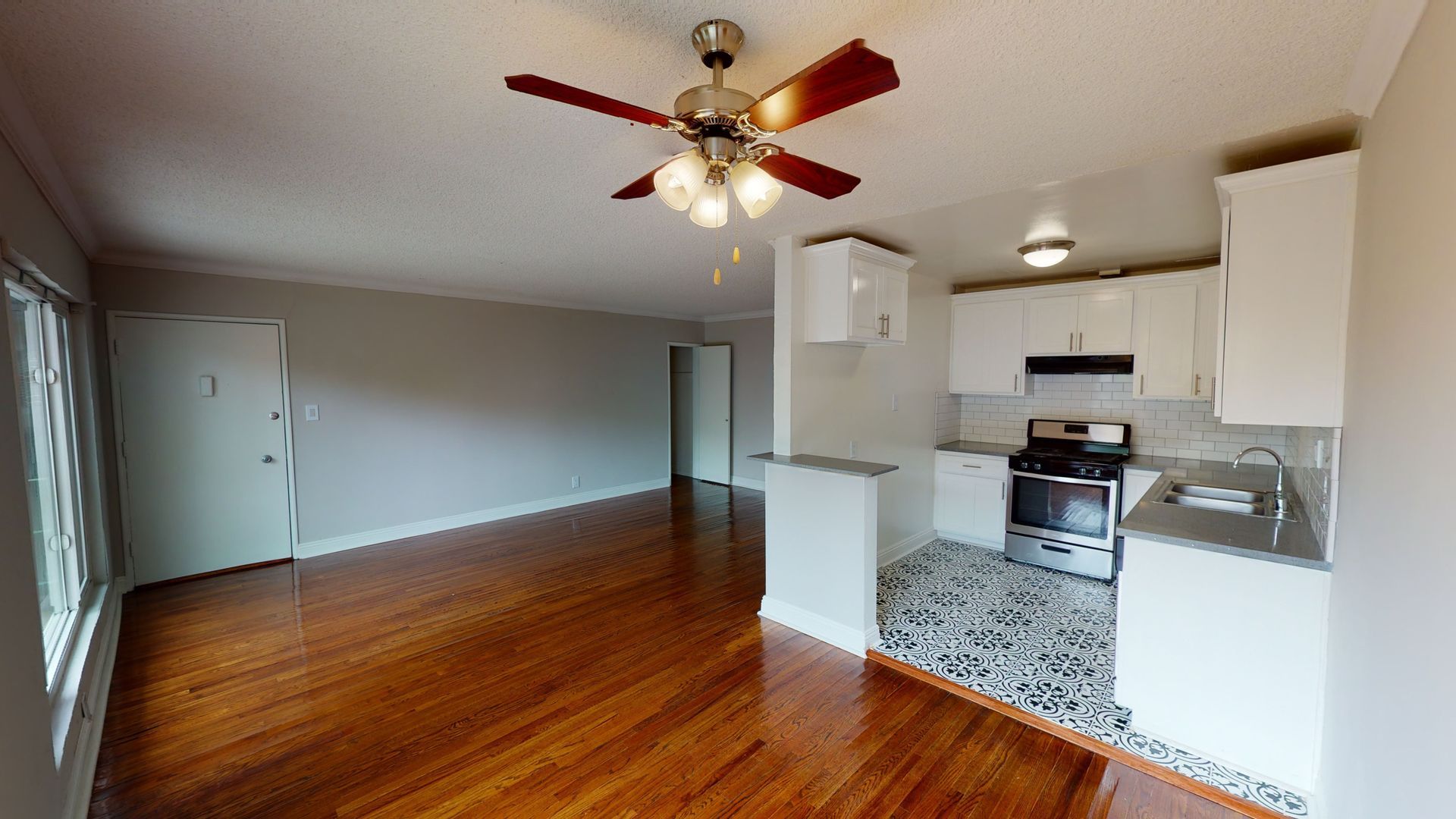 Spacious living area with hardwood floors, kitchen with white cabinets, and a ceiling fan.