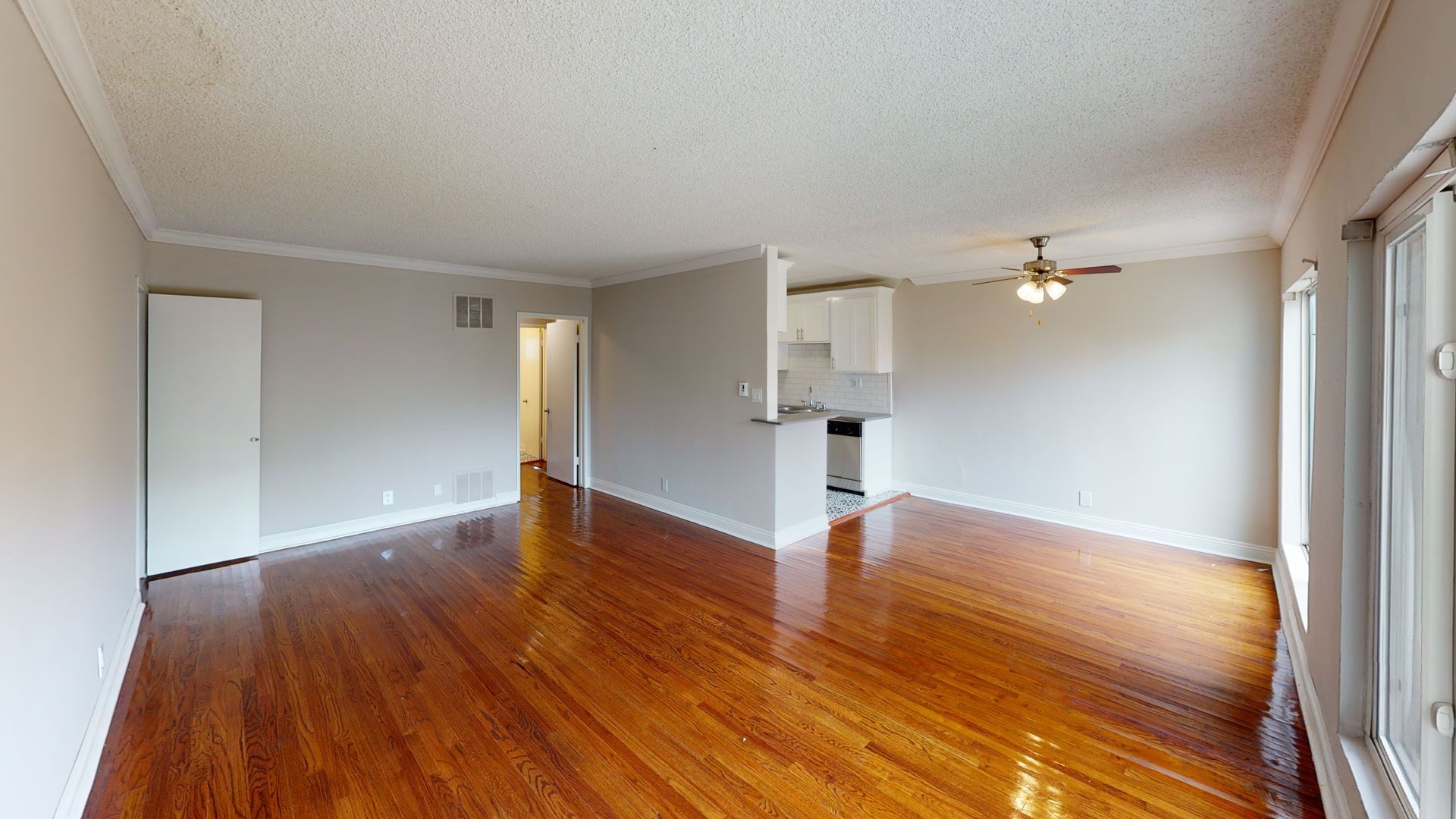 Empty apartment interior with wooden floors, white walls, and a small kitchen visible.