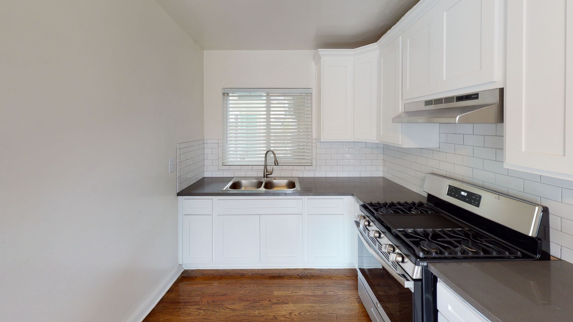 Small white kitchen with stainless steel appliances, dark countertops, and a window above the sink.