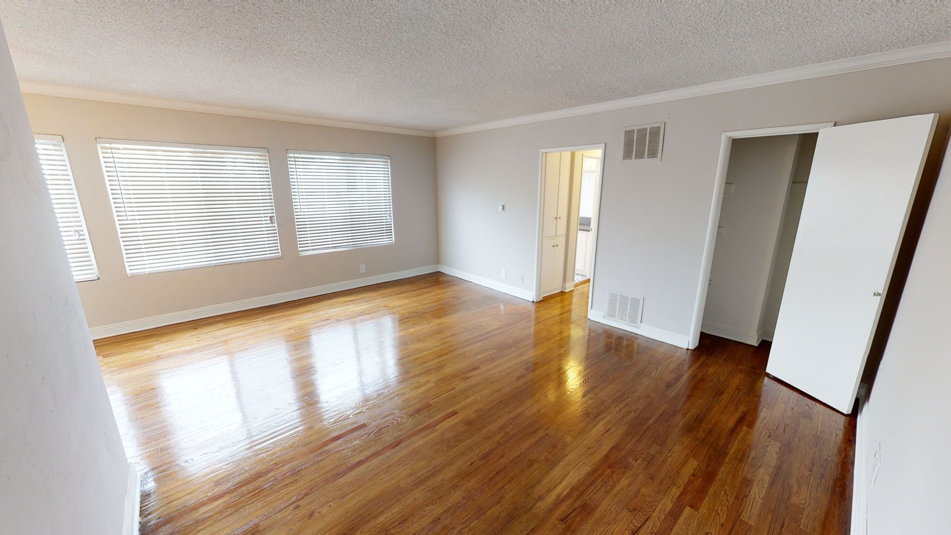 Spacious living room with hardwood floors and large windows. Includes doorways and a light fixture.