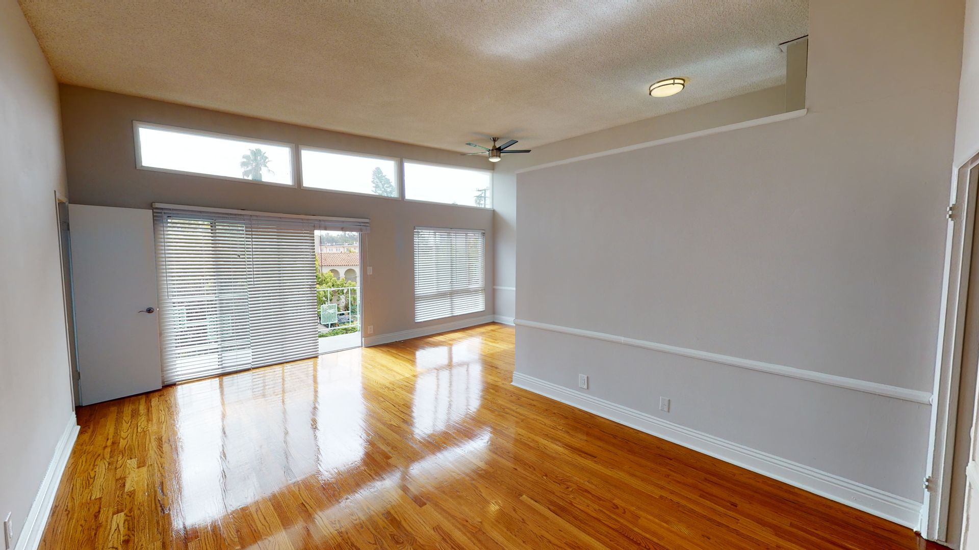 Bright living room with wood floors, large windows, and a door to a balcony.
