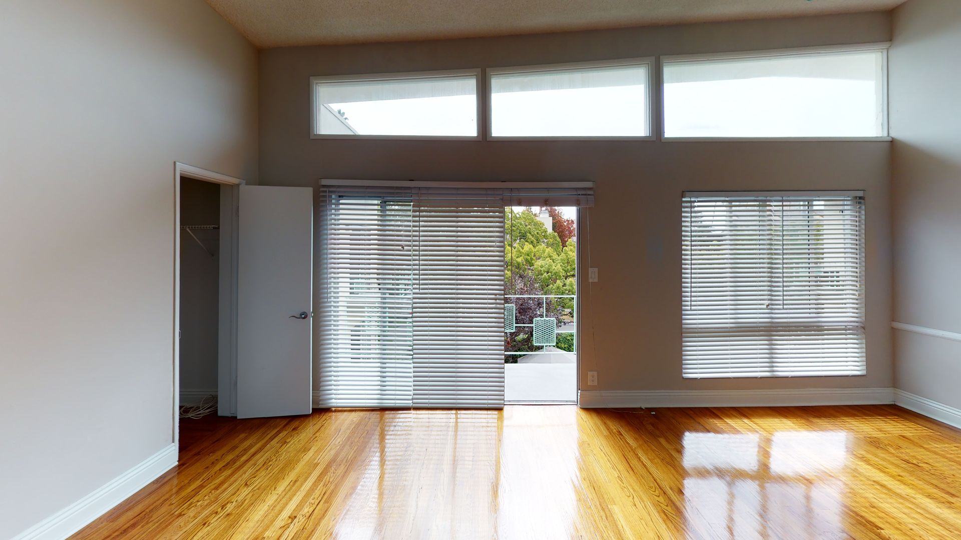 Empty room with hardwood floors, sliding glass doors to a patio, and high windows.