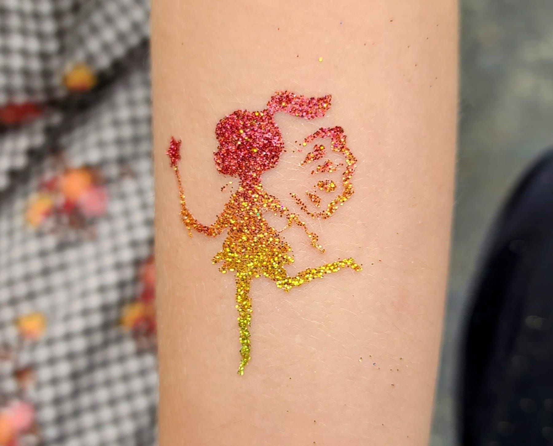 Glitter fairy tattoo in red and gold on an arm.