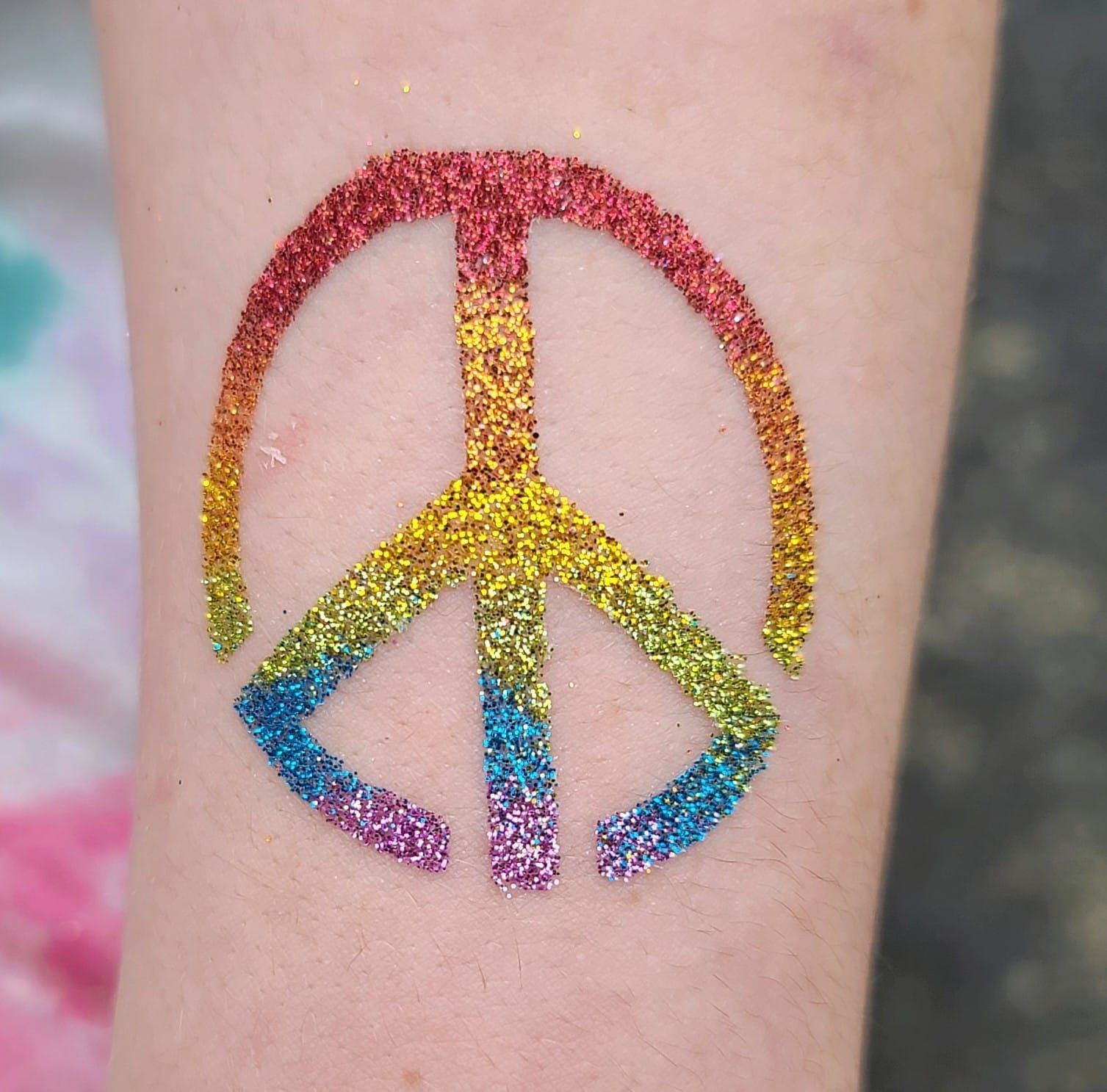 Glitter peace sign tattoo with rainbow gradient on fair skin.