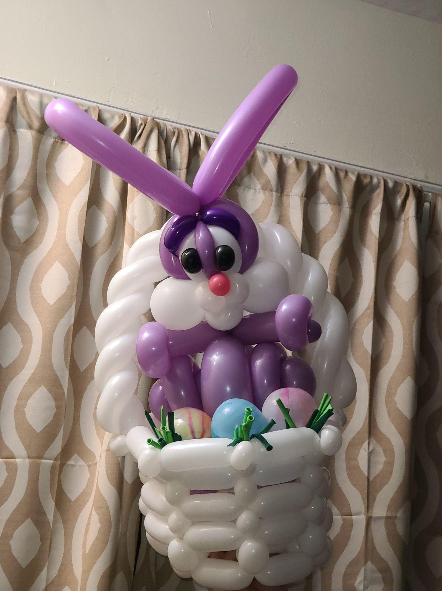 Man in purple holding a colorful balloon flower outdoors; smiling.